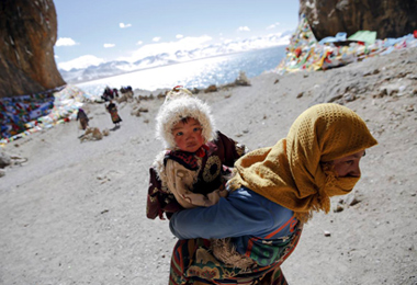 A well-dressed Tibetan woman carries his son to do Kora around Namtso Lake . 